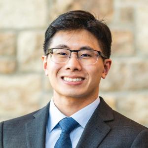 Ryan Kong wears a suit and blue tie and smiles at the camera for a photo