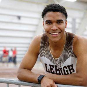 Skyler Mott leans against a track field fence wearing Lehigh track uniform