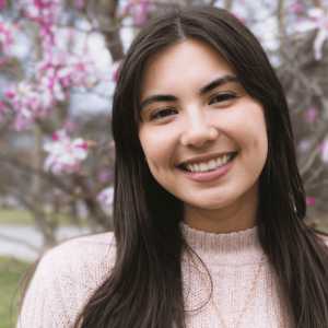 Maria Gregoire stands in front of a blooming magnolia tree wearing a pink sweater.