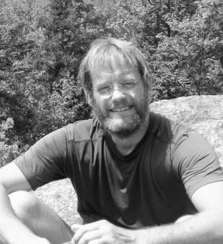 John Pettegrew sits on a side of a mountain and poses for a photo.