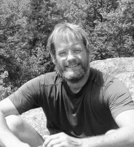 John Pettegrew sits on a side of a mountain and poses for a photo.