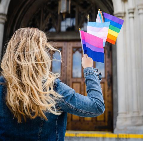 Abby Trainor holds three pride flags in her outstretched hand