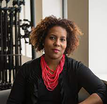 Salamishah Tillet poses for a photo wearing a black shirt and red necklace