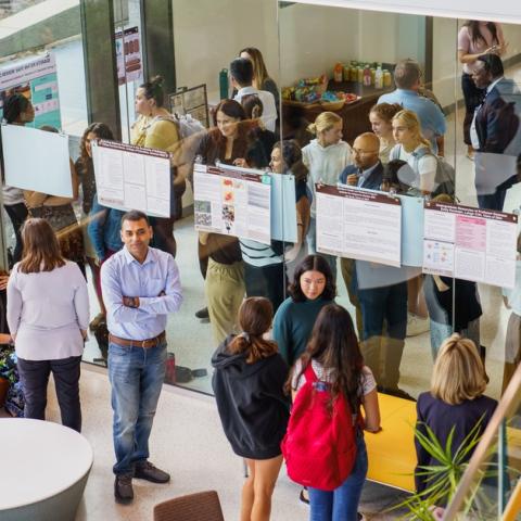 Research Symposium in the HST building. People mingle around posters on a wall.