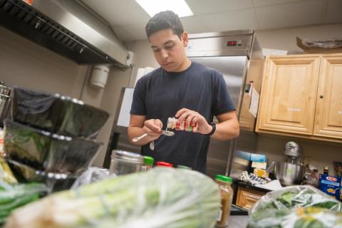 A student measures garlic powder in a kitchen.