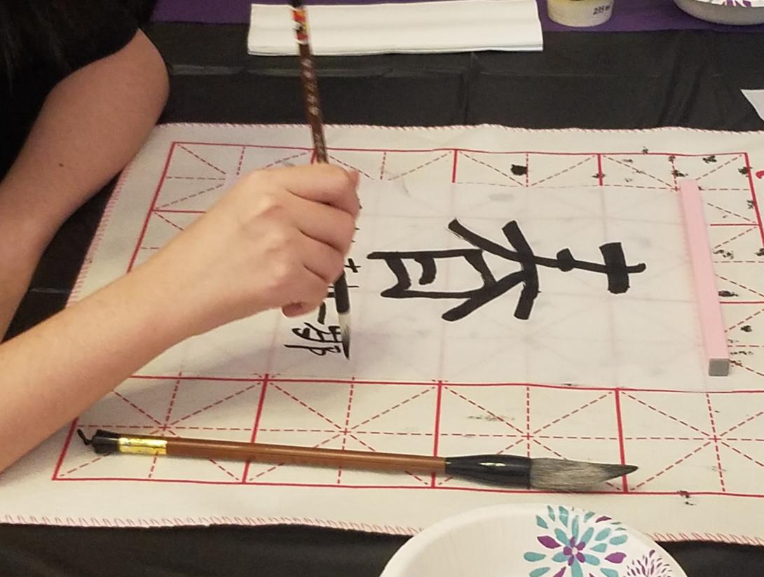 Student writes a Chinese word with a brush and black ink