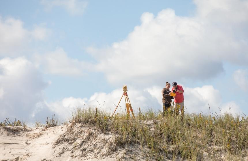 Frank J. Pazzaglia and student look at a paper on a dune