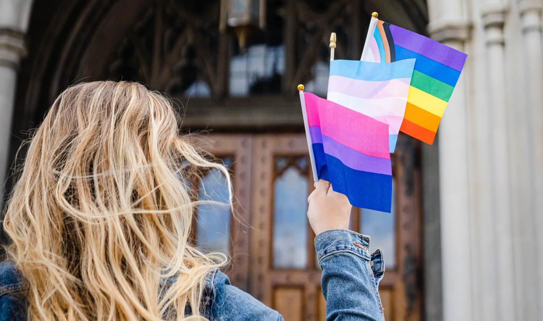 Abby Trainor holds three pride flags in her outstretched hand