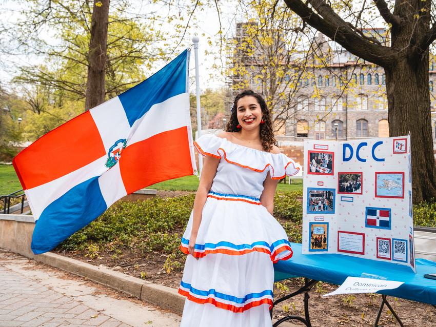 Estefania Ravelo Reyna standing at an information table representing Lehigh's Dominican Culture Club. The Dominican Republic flag is next to her.