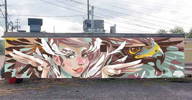 A picture of a mural on a building with a cartoon woman's face and a hawk