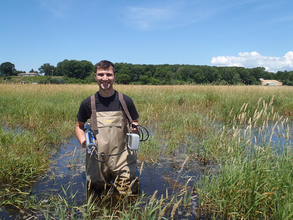 Eli Jacobson stands in a watery marsh holding equipment 