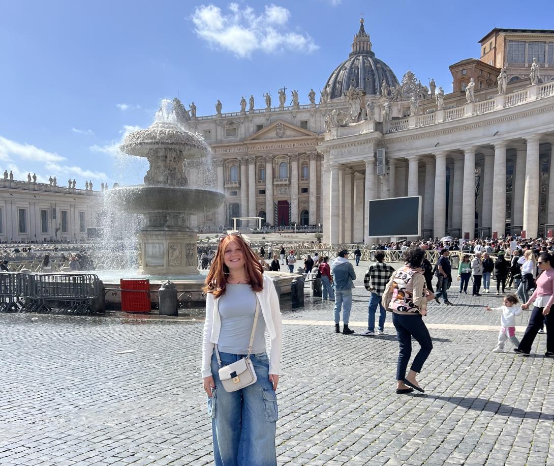 Julia Klayman stands in a courtyard in Rome, Italy with a fountain in the background