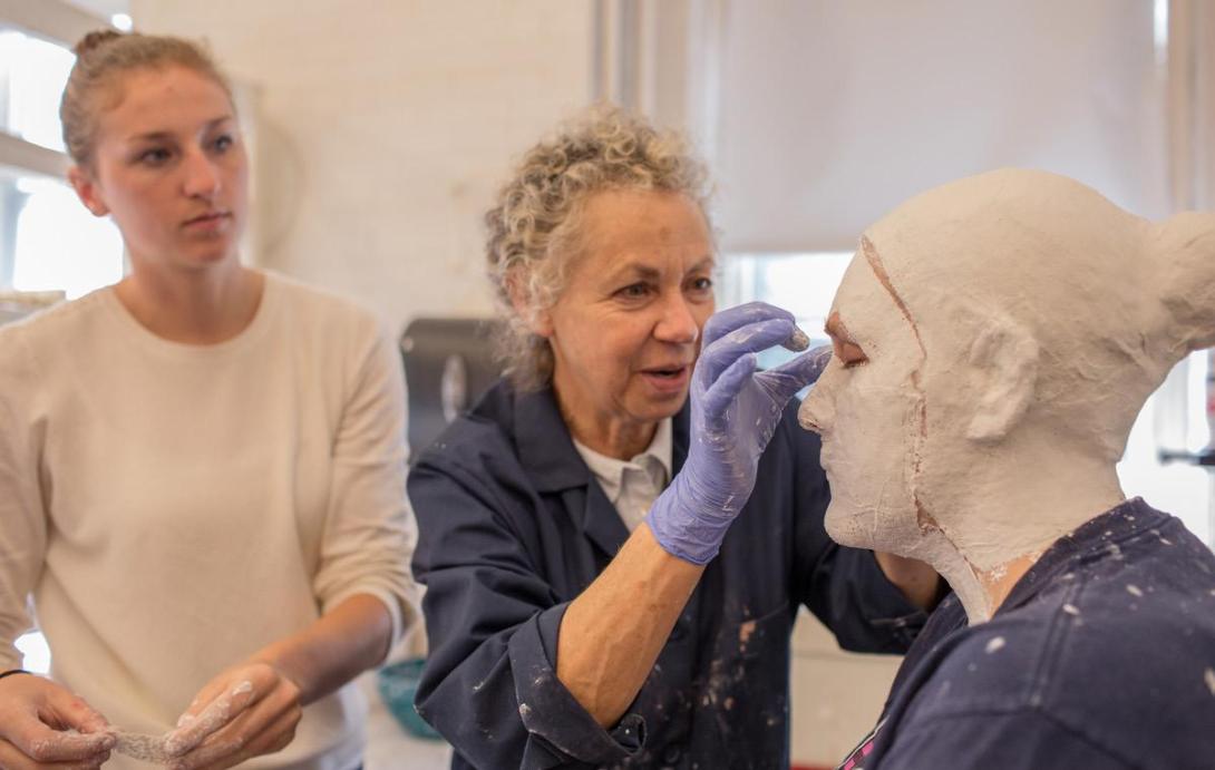 Lucy Gans puts plaster on a students head while another student observes