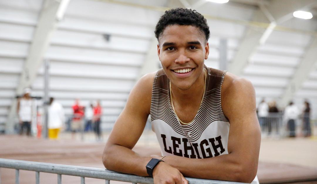 Skyler Mott leans against a track field fence wearing Lehigh track uniform