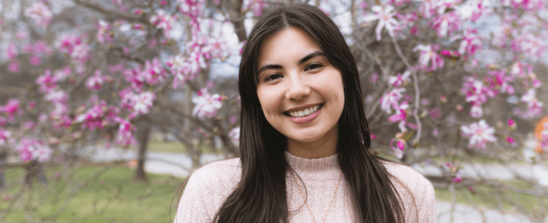 Maria Gregoire stands in front of a blooming magnolia tree wearing a pink sweater.