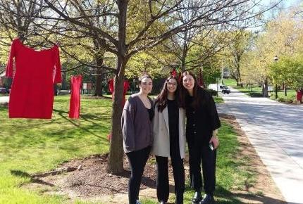 Students stand int he grass with red dress handing in the background.